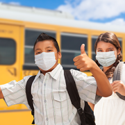 masked kids giving thumbs up in front of school bus
